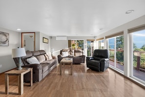 A spacious living room with a brown leather sofa, a black leather armchair, and a wooden coffee table.