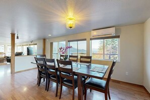 A dining area with a wooden table and chairs, large windows, and an air conditioning unit. - Gorge Retreat | Panoramic Views & Private Trail (Stevenson)