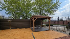 A covered outdoor seating area with a brick floor, a wooden pergola, and a metal fence. - Spacious & Classy Home for Extended Stays (Houston)