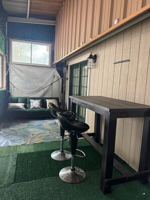 Una habitación con un sofá verde, una silla negra, una mesa de madera y una ventana con vista a árboles.