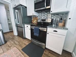 A modern kitchen with stainless steel appliances, white cabinetry, and a granite countertop.