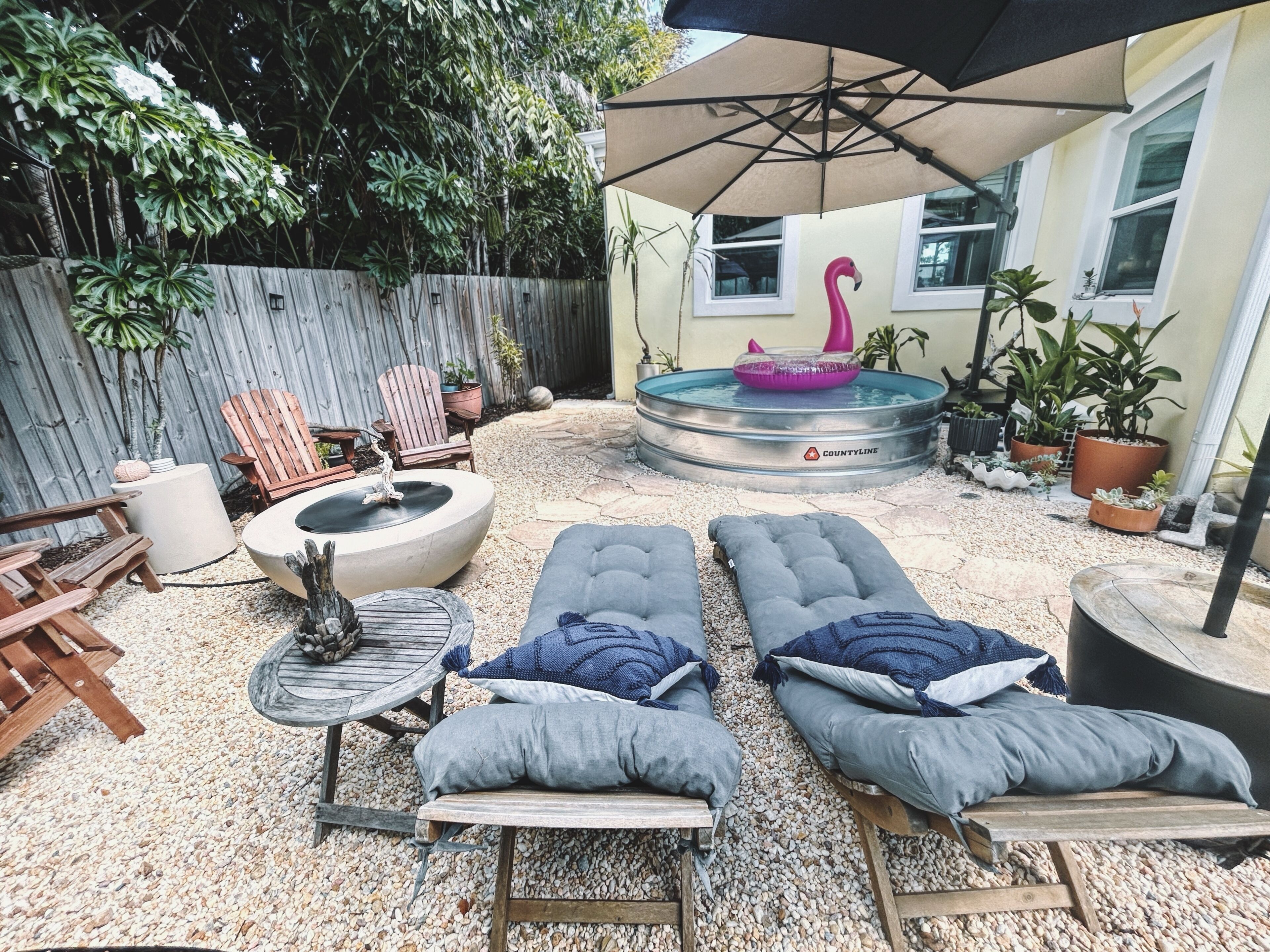 A backyard with a hot tub, lounge chairs, a wooden table, and a wooden fence.