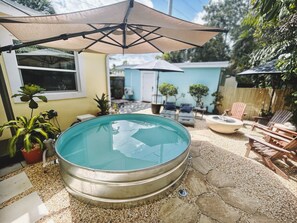Ein Schwimmbecken mit Metallrand, umgeben von einer Klinkerterrasse, Gartenmöbeln und Sonnenschirmen.