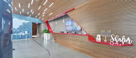 A modern reception area with a wooden slatted wall, a digital screen, and a Shabbat sign.