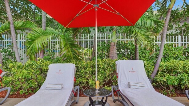 Deux chaises longues, un parasol rouge et une petite table placée entre elles.