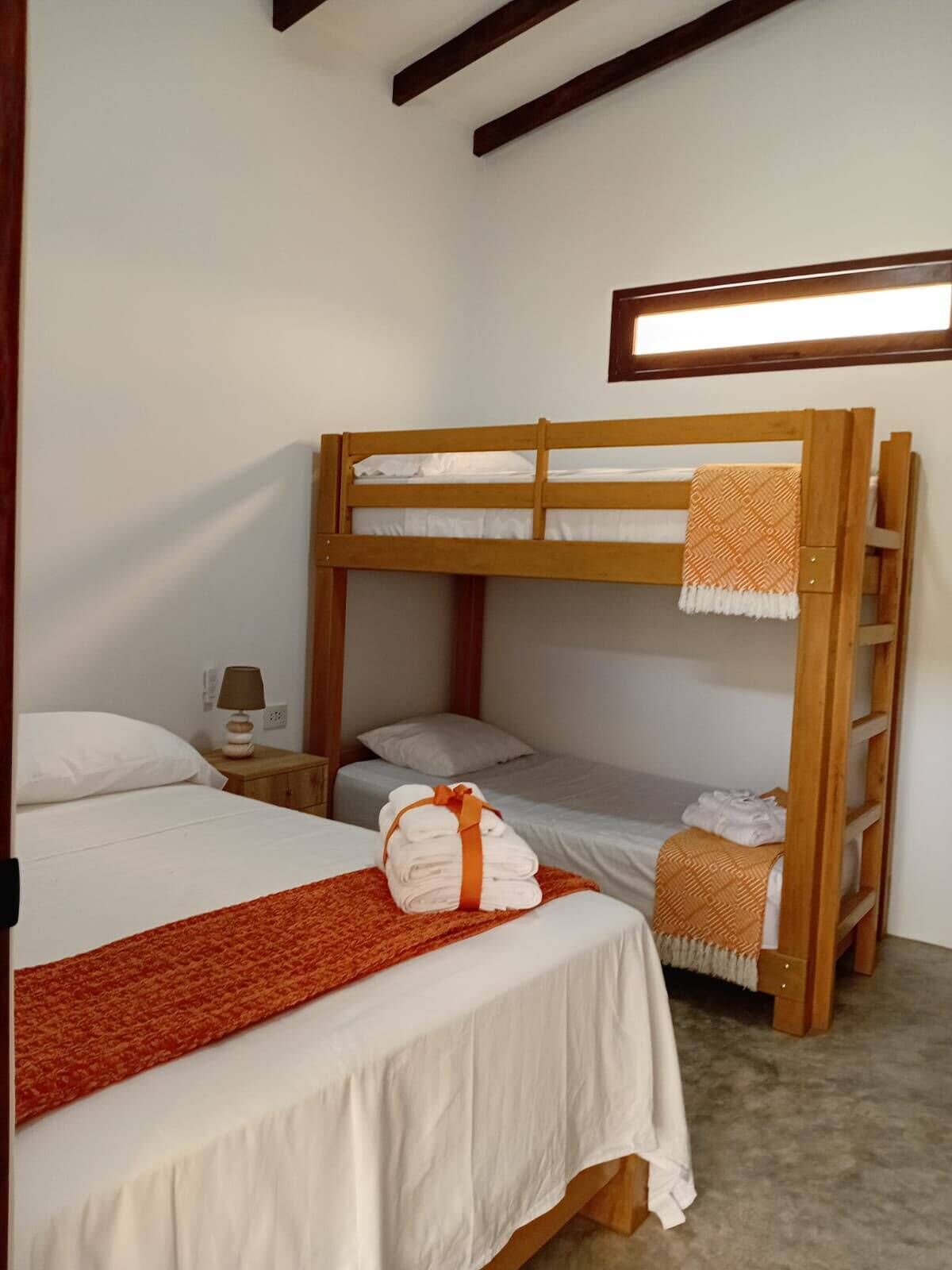 A bunk bed room with a wooden headboard, a bedside table with a lamp, and a red throw blanket.