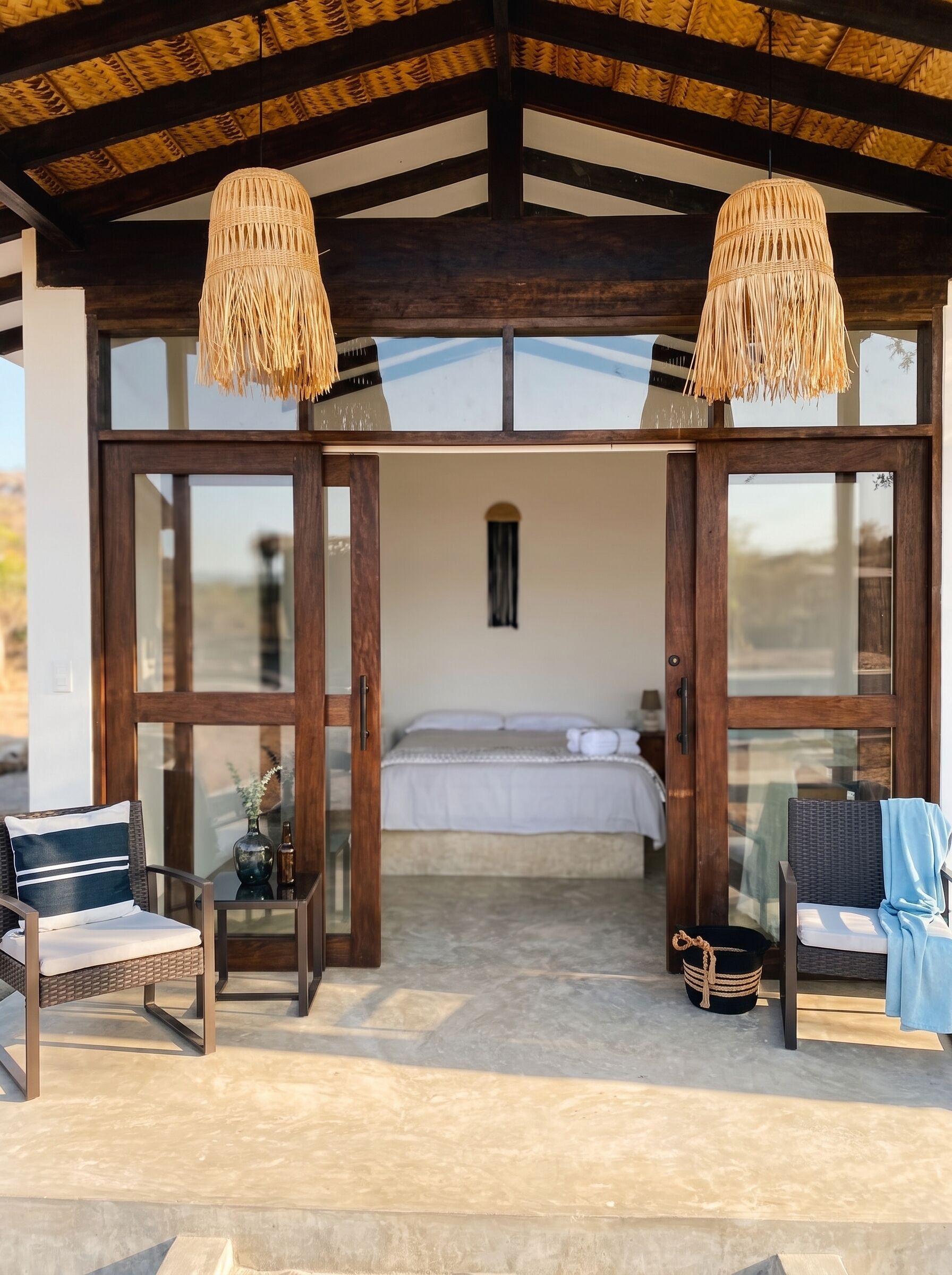 A room with a bed, two chairs, a small table, and a hanging light fixture.