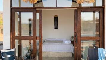 A room with a bed, two chairs, a small table, and a hanging light fixture.