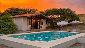 A swimming pool with a small building and umbrellas in the background.