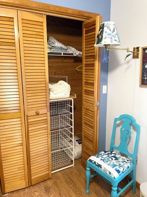 A wooden closet with a hanging rack, a small table, and a chair with a patterned cushion. - Sweet split level 4 bedroom house, quiet neighborhood, walking distance to beach (Kitty Hawk)