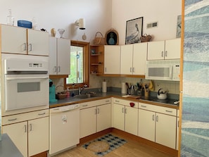 A kitchen with white cabinets, a microwave, a stove, and various kitchen utensils. - Sweet split level 4 bedroom house, quiet neighborhood, walking distance to beach (Kitty Hawk)