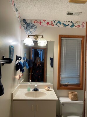 Ein Badezimmer mit Waschbecken, Spiegel, Handtuchhalter und einem Fenster mit Jalousien.