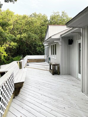 Een houten terras met een leuning, leidend naar een gebouw met witgekleurde gevelbekleding en een overdekte veranda.