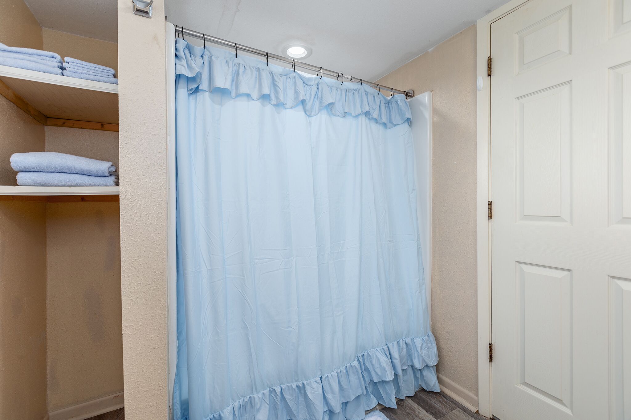 Een badkamer met douchegordijn, handdoekrek en deur.
