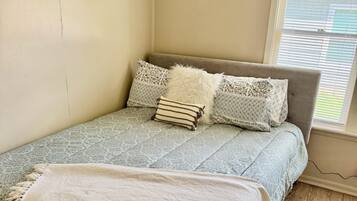 Una cama con ropa de cama estampada y almohadas, una manta blanca y una ventana con persianas.
