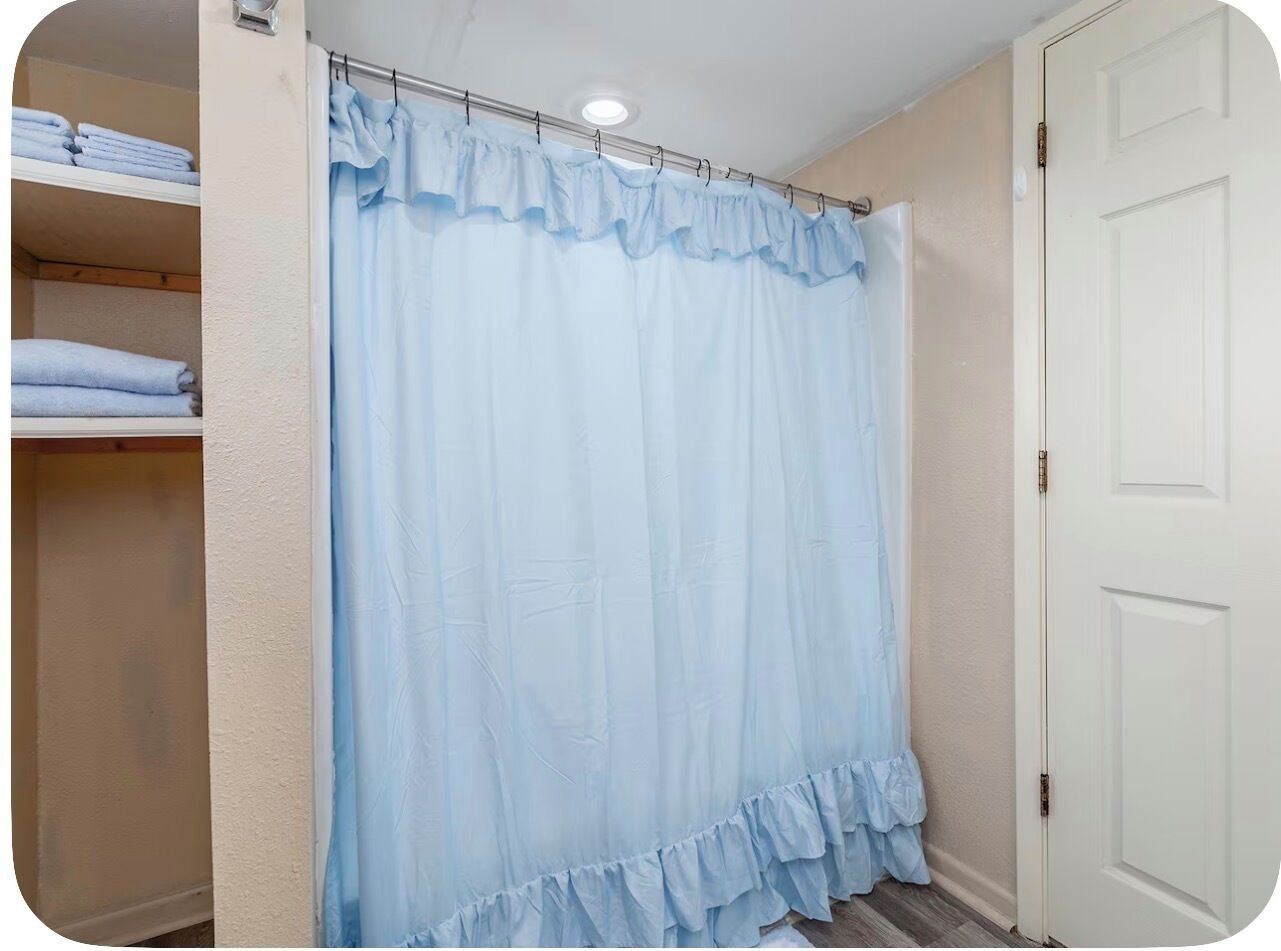 Um banheiro com cortina de chuveiro, uma porta e um prateleira com toalhas dobradas.