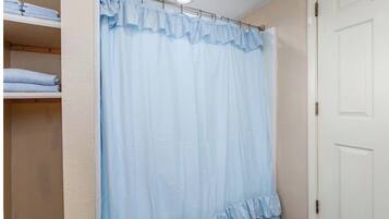 Um banheiro com cortina de chuveiro, uma porta e um prateleira com toalhas dobradas.