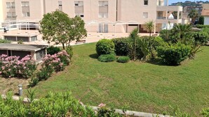 Un edificio residencial con techo plano, un espacio al aire libre cubierto para sentarse y un césped bien cuidado con arbustos variados y un árbol.