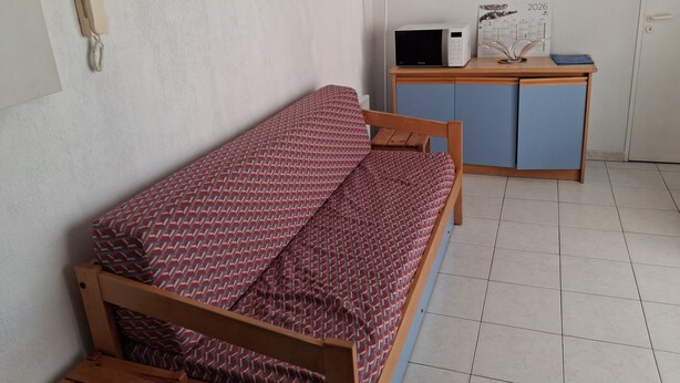 Habitación pequeña con una cama individual, un escritorio con ordenador y teléfono en la pared.
