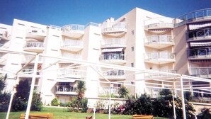 Un edificio residencial de varios pisos con balcones, un espacio al aire libre cubierto y un jardín con bancos.
