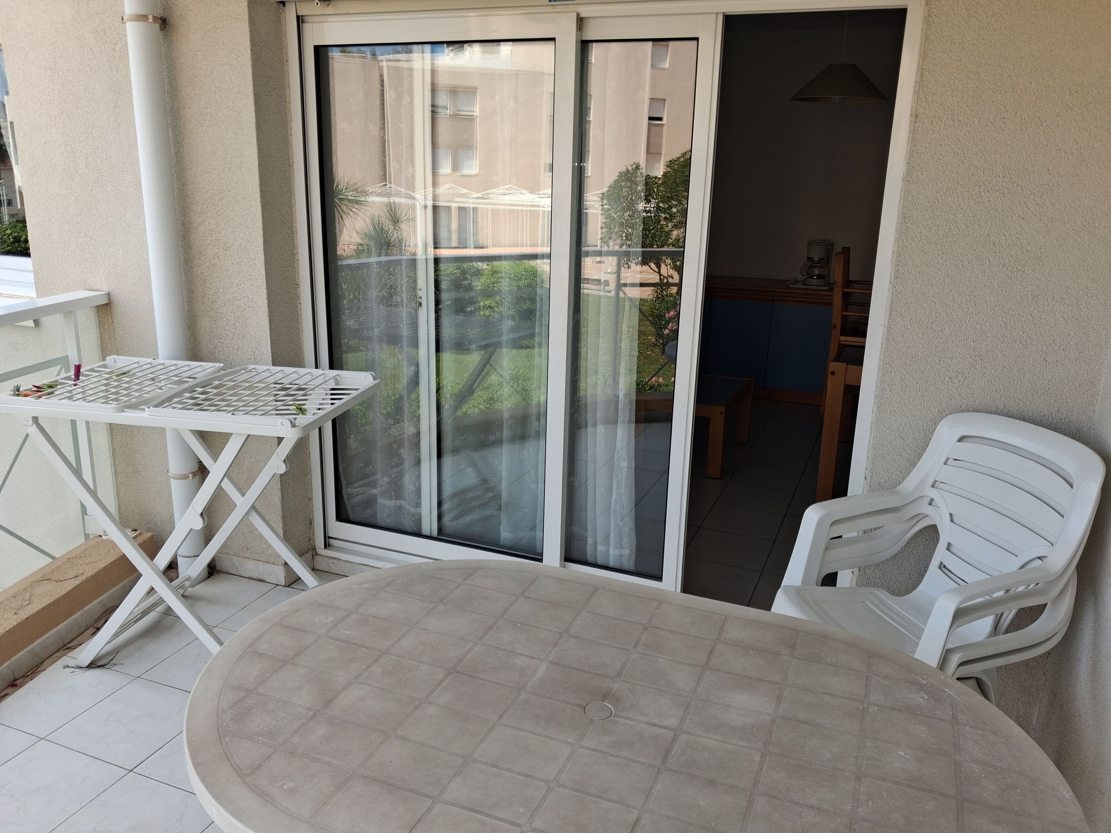 Un balcon avec une table et des chaises, une porte-fenêtre coulissante et une vue sur un immeuble et de la verdure.