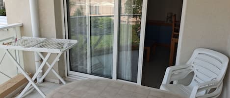 A balcony with a table and chairs, a sliding glass door, and a view of a building and greenery.