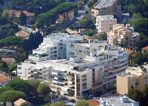 A multi-story residential building with balconies, surrounded by trees and other buildings.