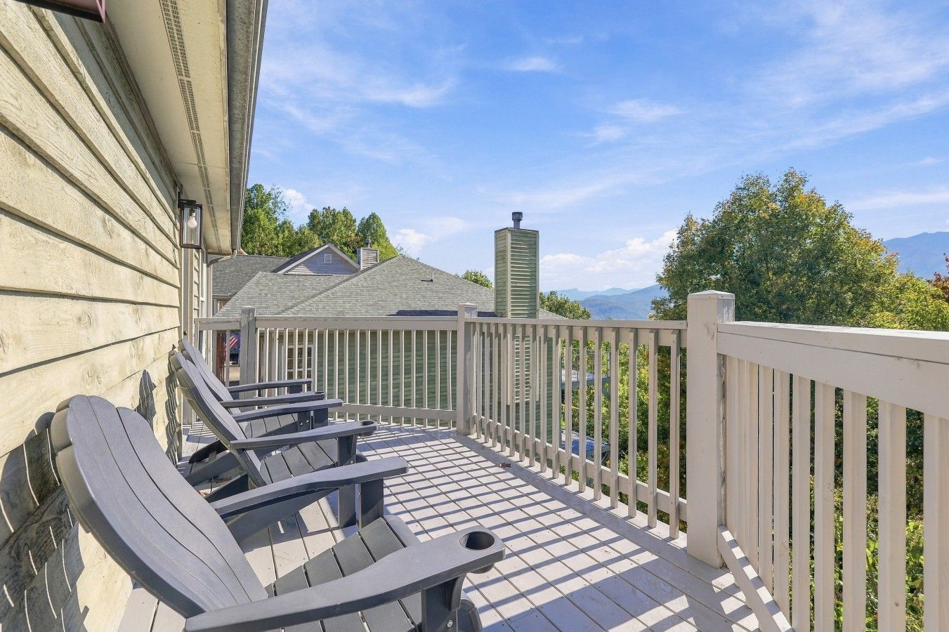 Un patio in legno con poltrone Adirondack e un parapetto bianco, con vista su un paesaggio montano.
