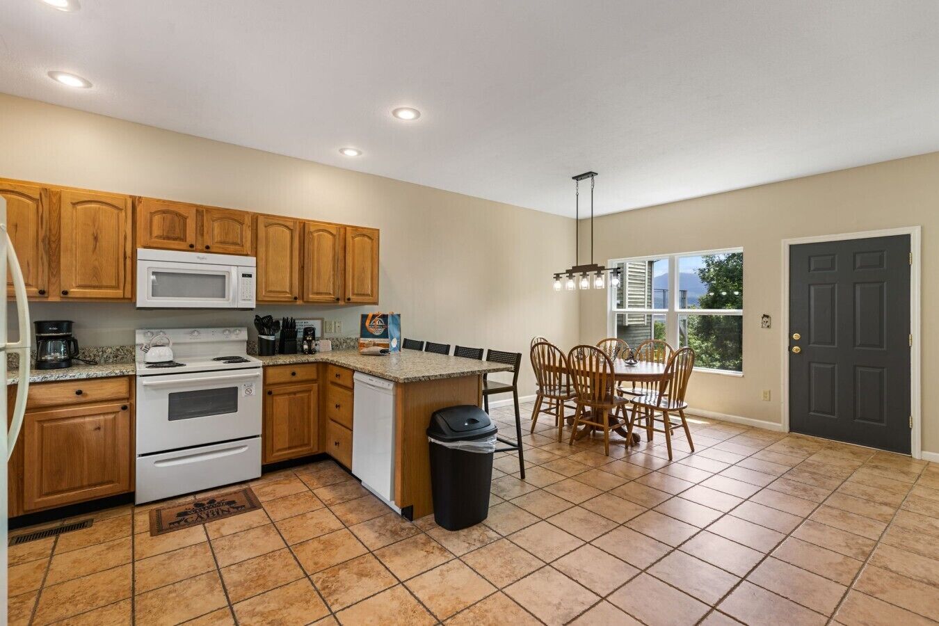 A kitchen with wooden cabinets, a microwave, stove, and a dining area with a table and chairs.