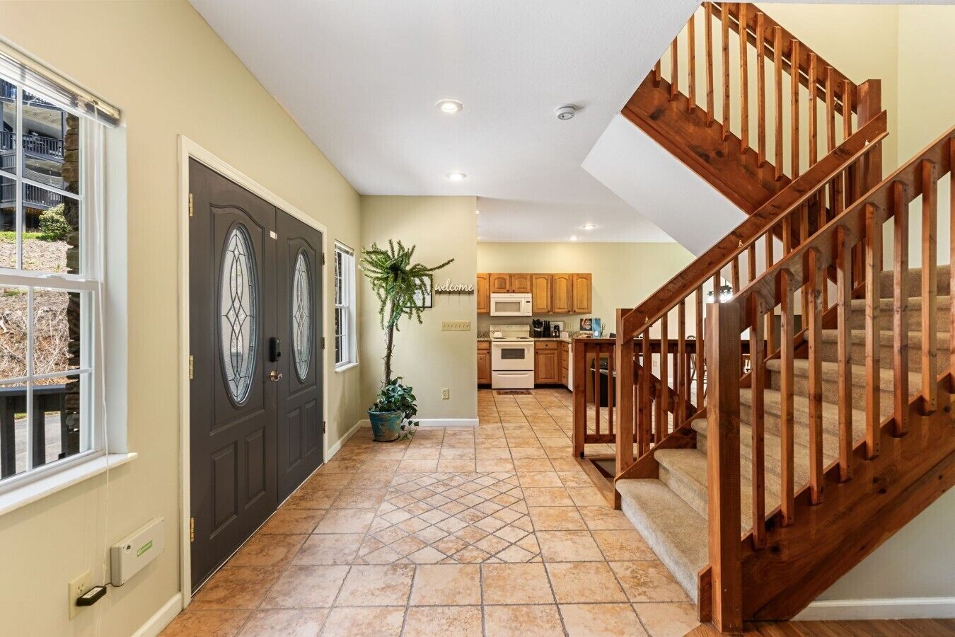 A home interior with a dark front door, a wooden staircase, a kitchen with wooden cabinets, and a potted plant.