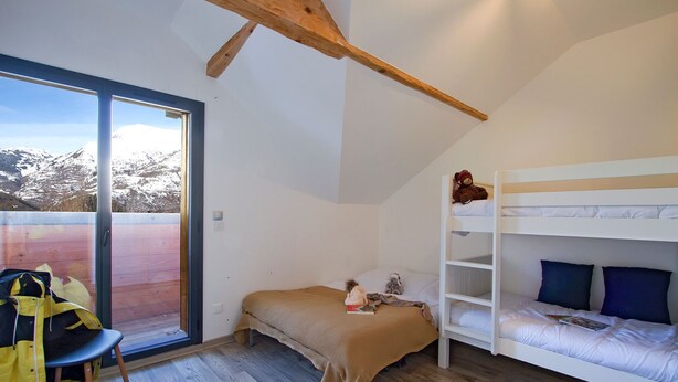 Ein Zimmer mit einem Etagenbett, einem Sessel, einem Tisch und Blick auf einen verschneiten Berg.