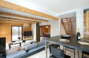 A modern interior with a dining area, a sofa, a TV, and a bottle of champagne. - Chalet rénové à 150 m du télésiège | Vue montagne (Mont-de-Lans)