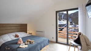Ein Schlafzimmer mit einem Bett, einem Sessel, einem Teddybären und Blick auf eine verschneite Landschaft durch ein großes Fenster.