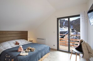 A bedroom with a bed, a chair, a teddy bear, and a view of a snowy landscape through a large window. - Chalet rénové à 150 m du télésiège | Vue montagne (Mont-de-Lans)