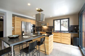 A modern kitchen with a central island, stainless steel appliances, and a large window providing natural light. - Chalet rénové à 150 m du télésiège | Vue montagne (Mont-de-Lans)