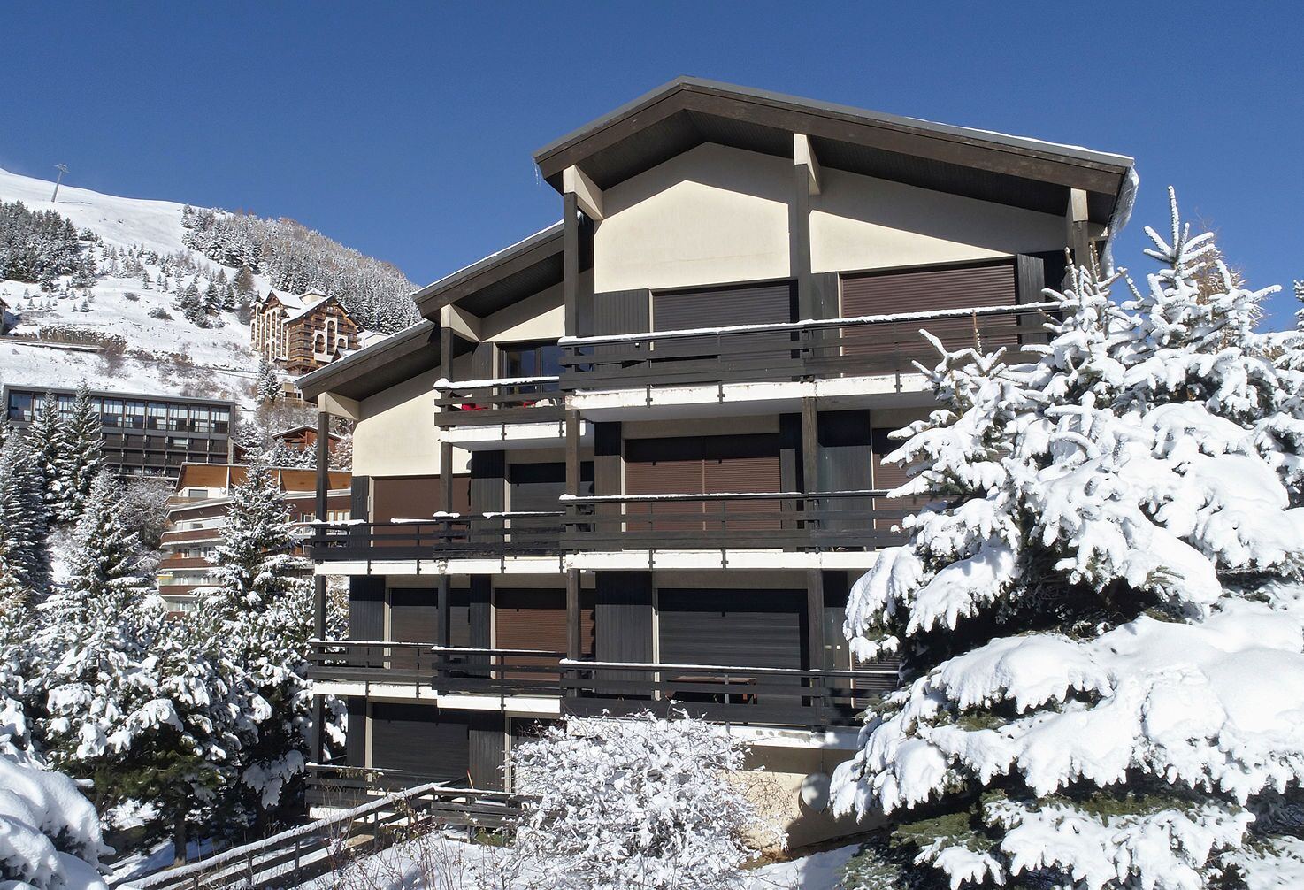 Un hotel de varios pisos con balcones, rodeado de árboles cubiertos de nieve y un cielo despejado.