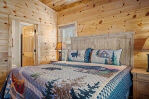 Ein Schlafzimmer einer Holzhütte mit einem Bett, einem Nachttisch, einer Lampe und einer Tür.