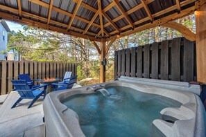 Ein Whirlpool mit Holzterrasse und blauen Stühlen, umgeben von einem Holzzaun und Bäumen.