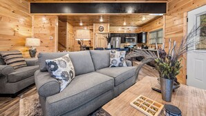 Een gezellige woonkamer met een grijze bank, gestreepte kussens en een salontafel met een afstandsbediening en decoratieve objecten.