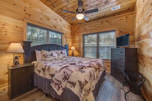 A wooden cabin bedroom with a bed, nightstands, a dresser, a ceiling fan, and two windows with blinds. - Smokies Modern Cabin Fireplace, Fire Pit, Games! (Pigeon Forge)
