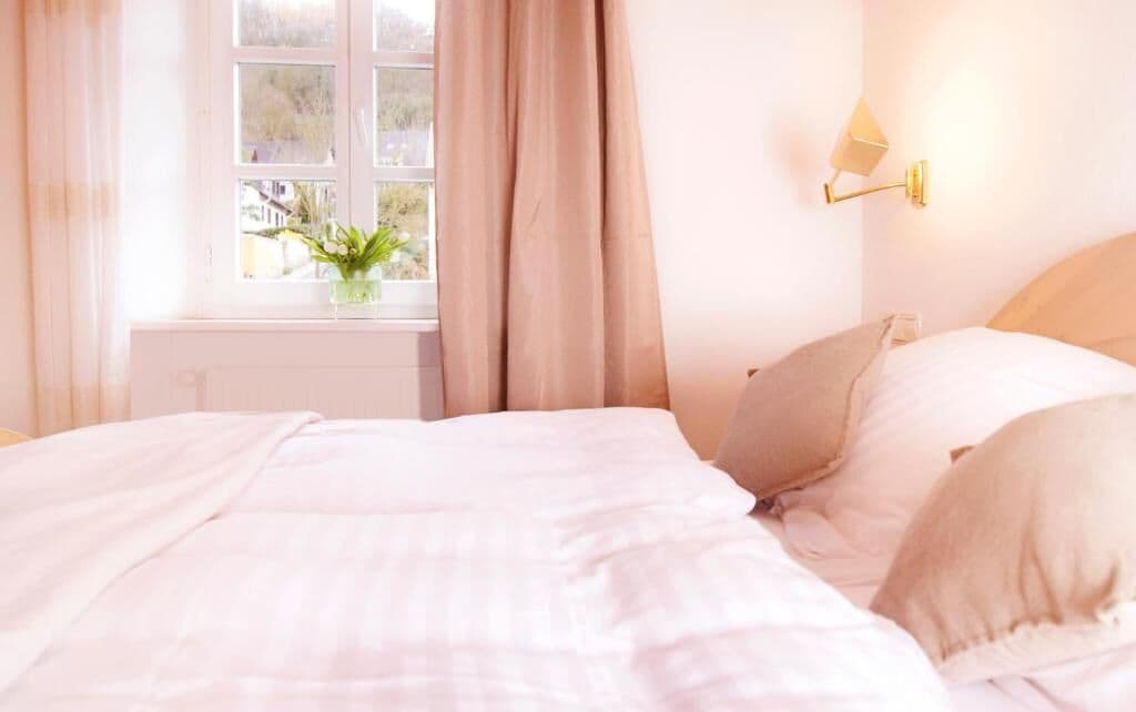 Un dormitorio con cama, ventana con cortinas, lámpara de noche y una planta en maceta.