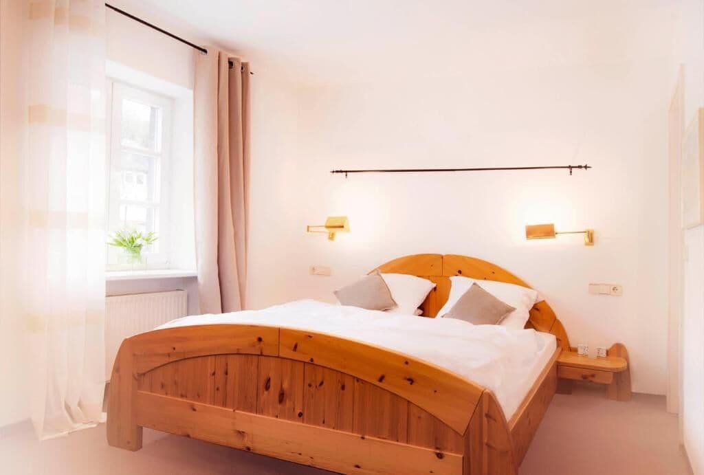A room with a wooden bed, bedside lamps, and a window with curtains.