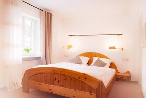 Huoneessa on puinen sänky, yöpöydällä lamput ja ikkunassa verhot.