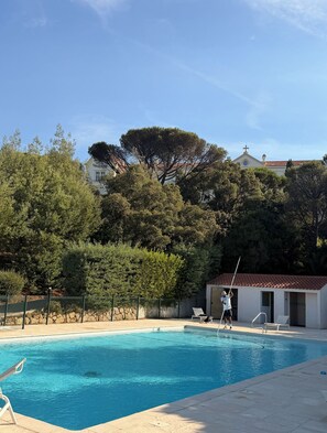A swimming pool with a clear blue water surface, surrounded by trees and a building with a red-tiled roof. - Adorable studio with AC in charming La Croix-Valmer (La Croix-Valmer)