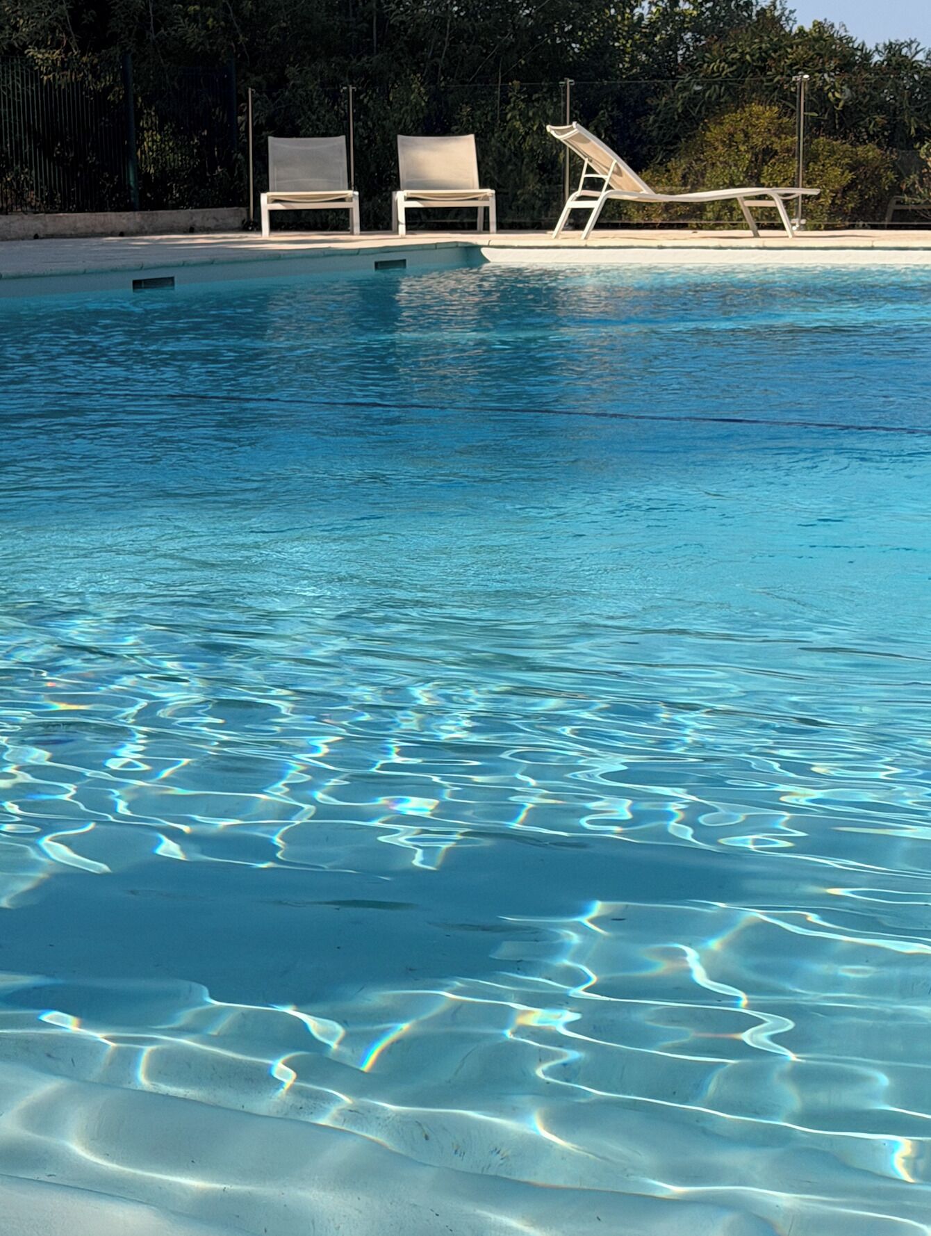 A clear swimming pool with three lounge chairs and a sunbed.