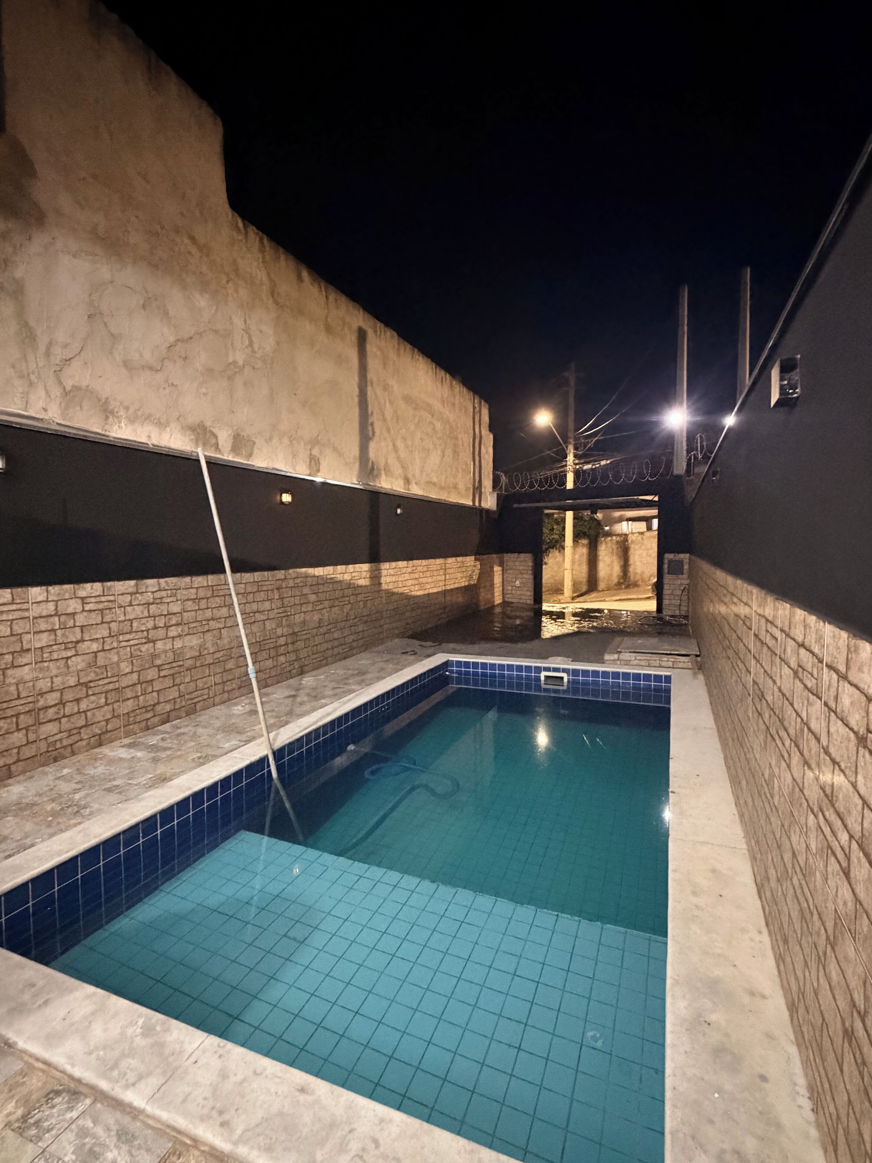 Une piscine dont les bords sont recouverts de carreaux, entourée de murs avec un motif en briques et dotée d’un sol en béton.