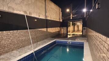 Une piscine dont les bords sont recouverts de carreaux, entourée de murs avec un motif en briques et dotée d’un sol en béton.