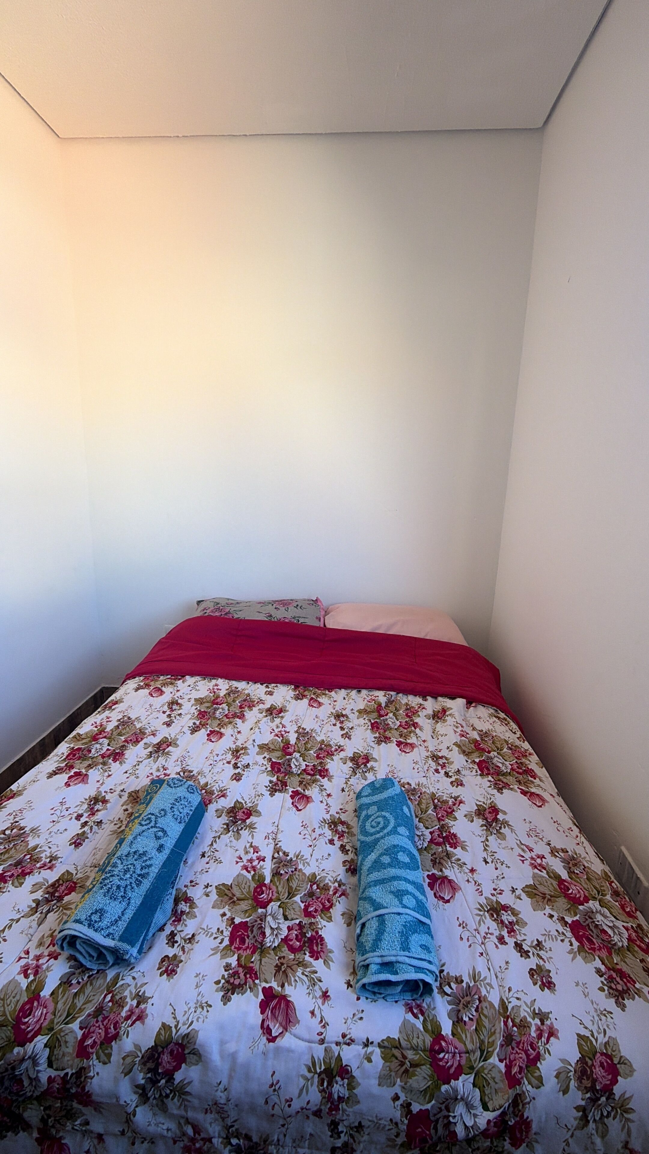 Un lit simple avec une couvre-lit à motifs floraux et deux serviettes enroulées.
