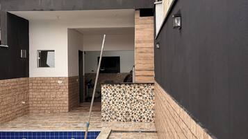 Una piscina amb un solàrium enrajolat, una paret de maó i un edifici modern amb terrat pla.