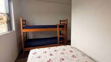 Une chambre avec un lit superposé, un lit simple avec une literie à motifs floraux, une fenêtre et un plafond blanc.